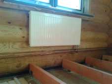 Монтаж отопления загородного дома. Панельный радиатор на стене из оцилиндрованного бревна. Обвязка открытыми медными трубами
